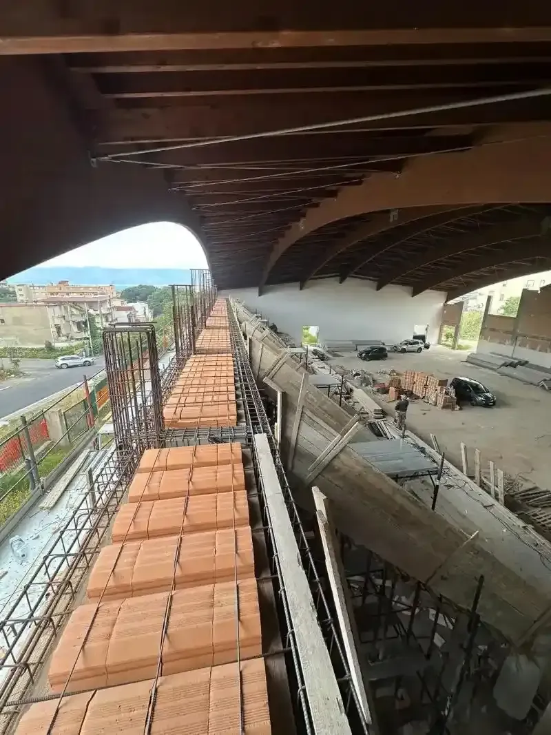 Cantiere sotto un ponte; operai, cemento, mattoni e impalcature.