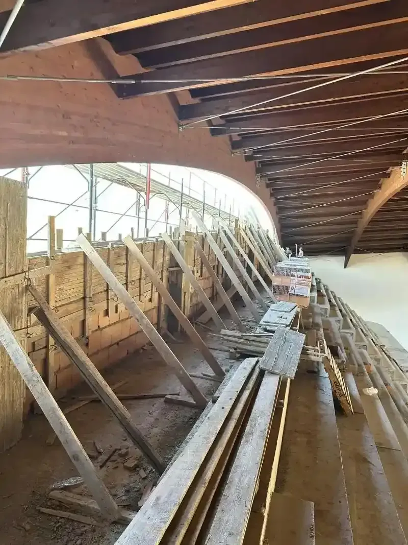 Vista interna del cantiere. Un'impalcatura in legno sostiene il soffitto a volta; assi sul pavimento.