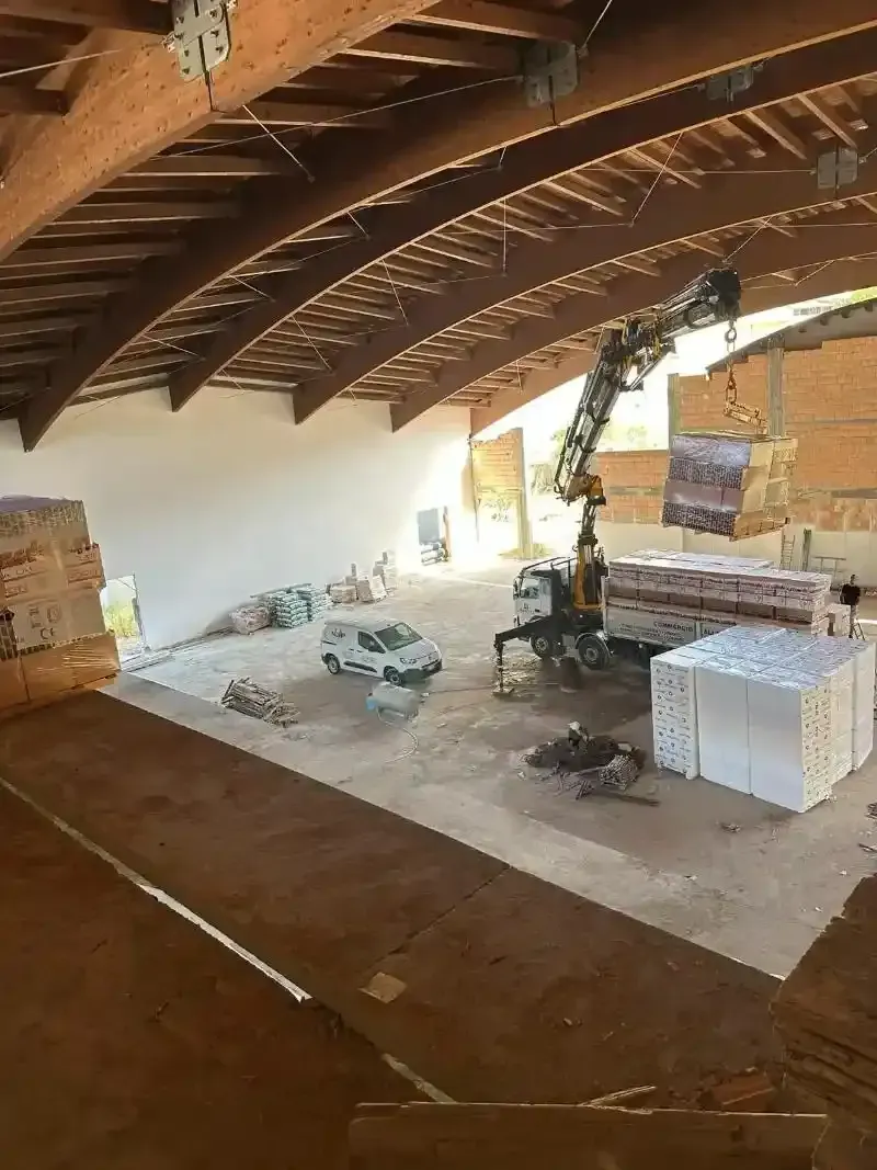 Cantiere edile: gru che scarica materiali in un edificio con travi di legno curve.