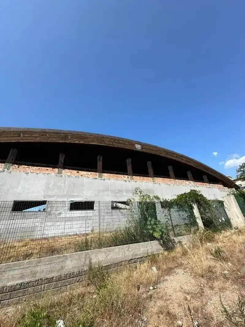 Vista esterna di un edificio con tetto curvo in costruzione contro un cielo azzurro terso.