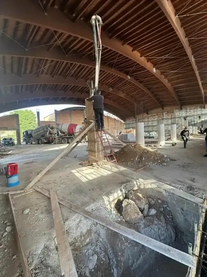 Cantiere con operaio su impalcatura che versa calcestruzzo con una pompa.