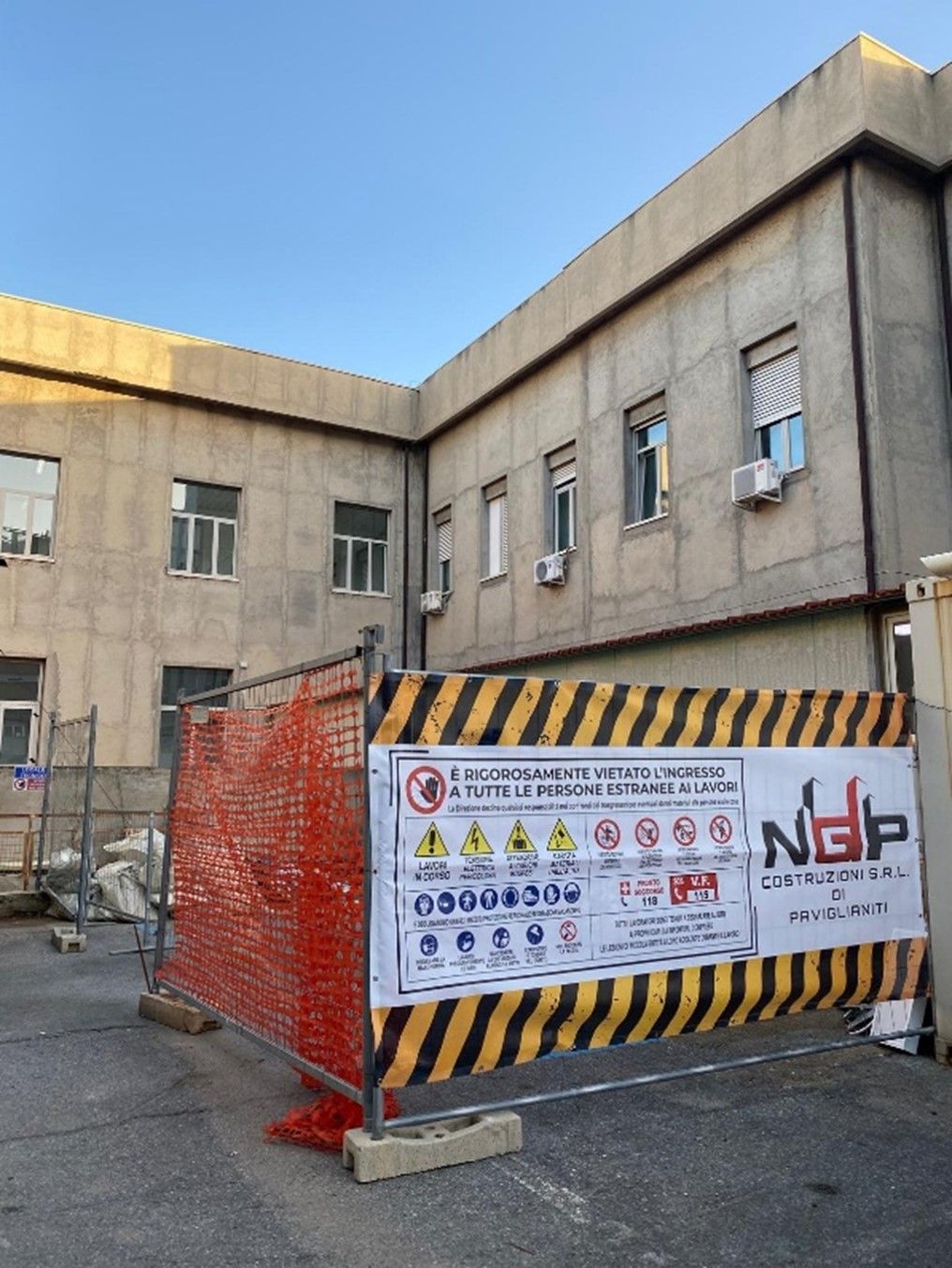 Vista stradale: marciapiede in cemento accanto all'edificio, materiali da costruzione, auto parcheggiate sulla strada.