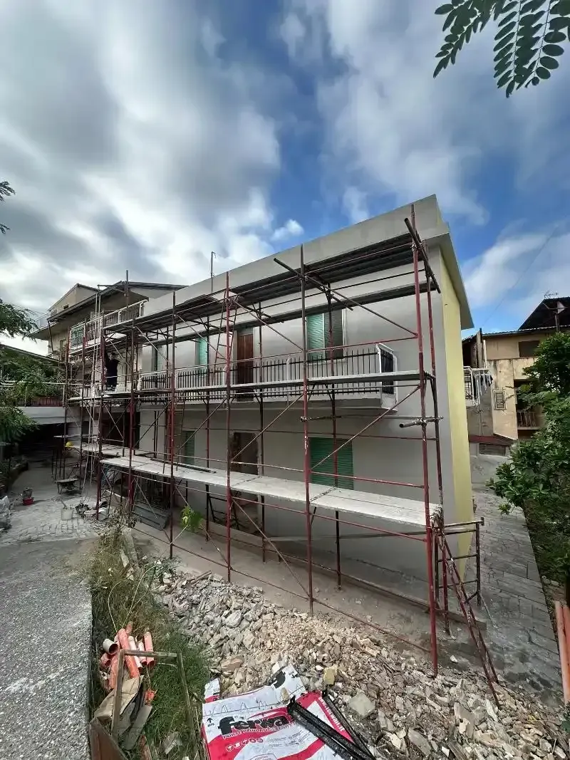 Esterno dell'edificio con impalcature per la ristrutturazione; cielo coperto.