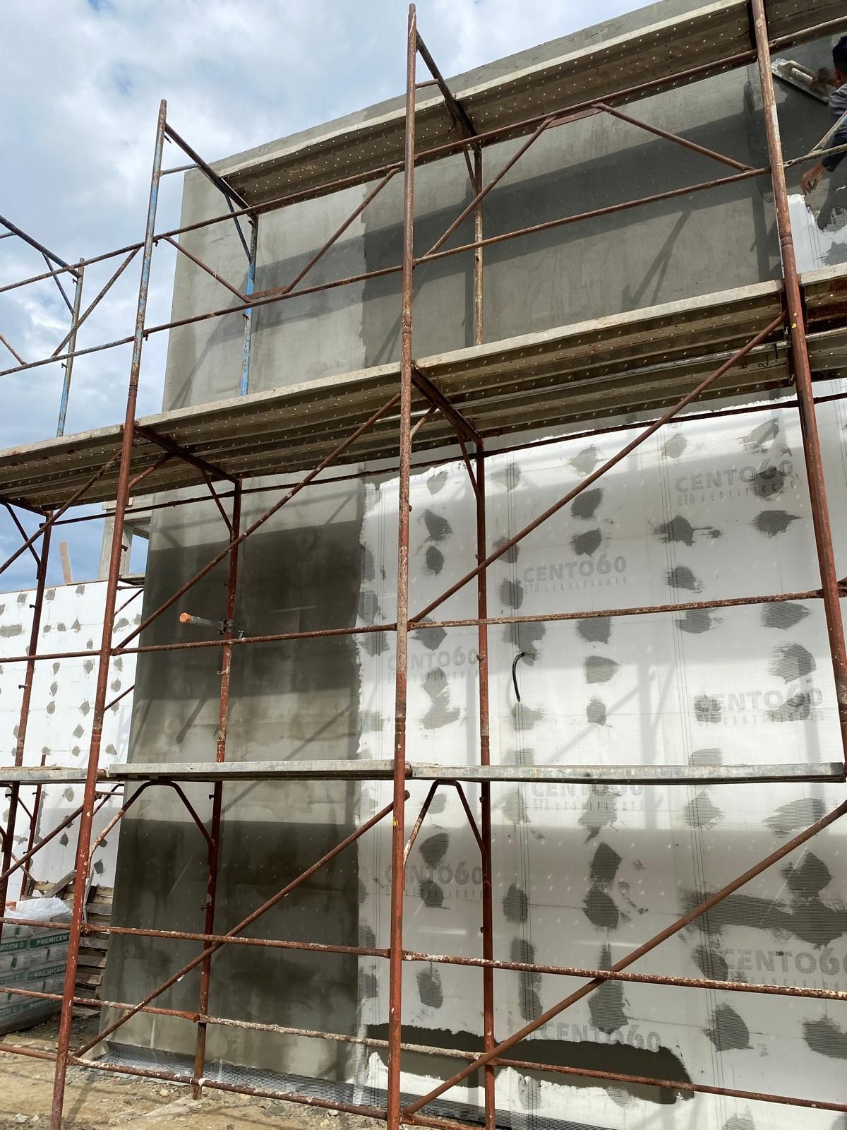 Operai su un'impalcatura che applicano lo stucco all'esterno di un edificio.