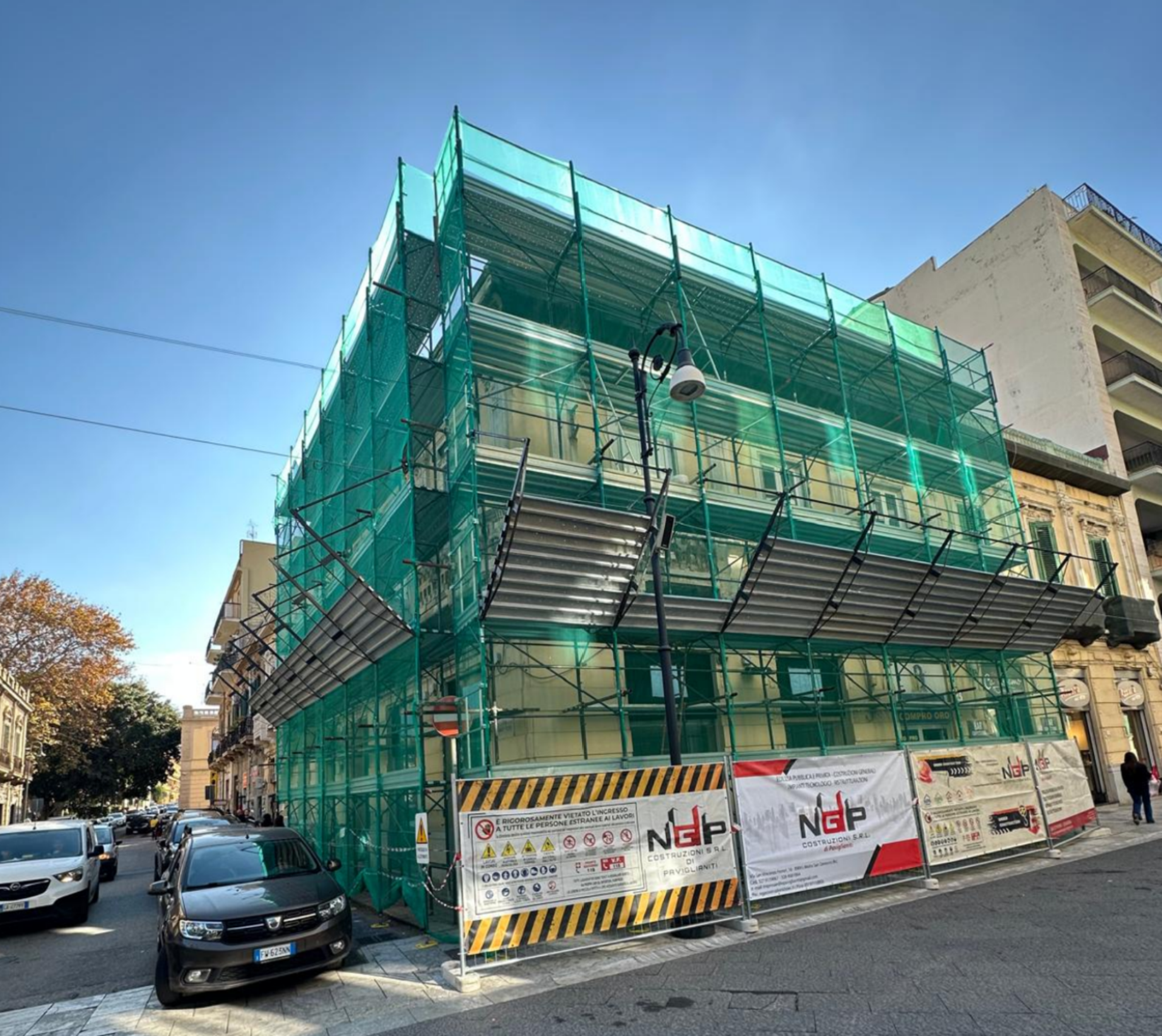 Lungo corridoio con pavimento in legno, pareti bianche e numerose porte chiuse.