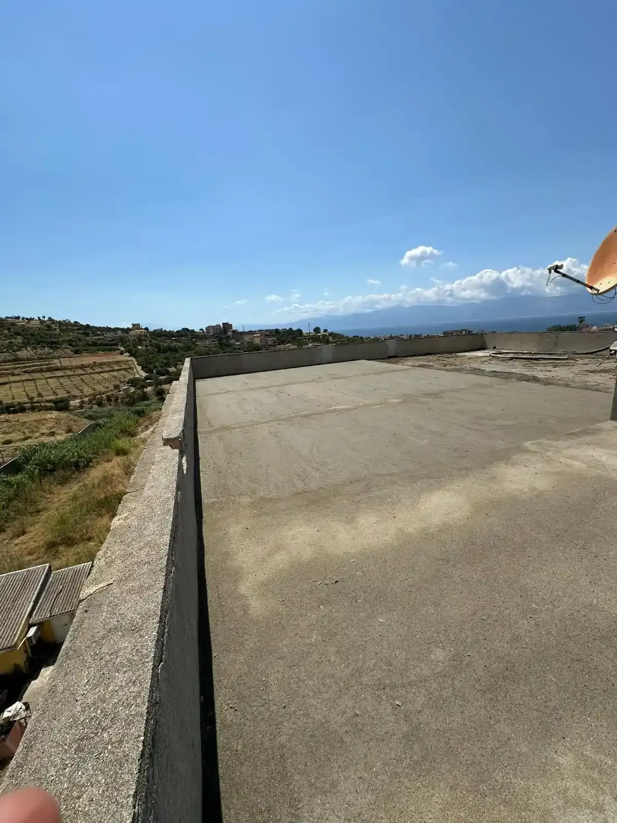 Un tetto in cemento con vista su una collina, montagne in lontananza e cielo azzurro.