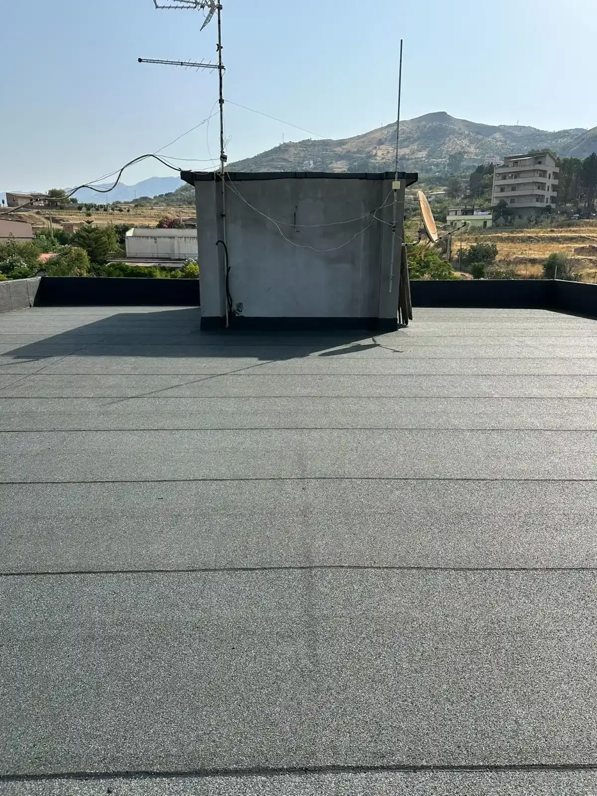 Tetto piano con una piccola struttura in cemento, antenna e montagne sullo sfondo.