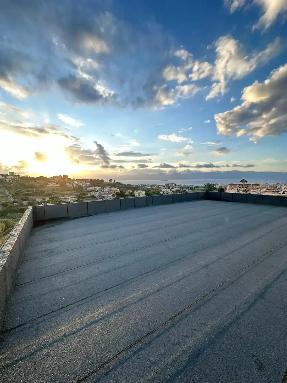 Vista dal tetto al tramonto, con vista sul paesaggio urbano verso l'oceano, sotto un cielo parzialmente nuvoloso.