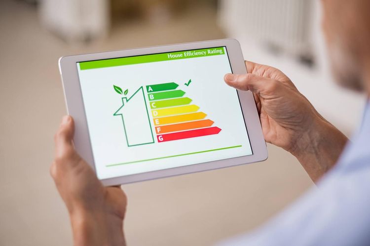 Persona che tiene in mano un tablet che mostra un grafico di valutazione dell'efficienza energetica di una casa.