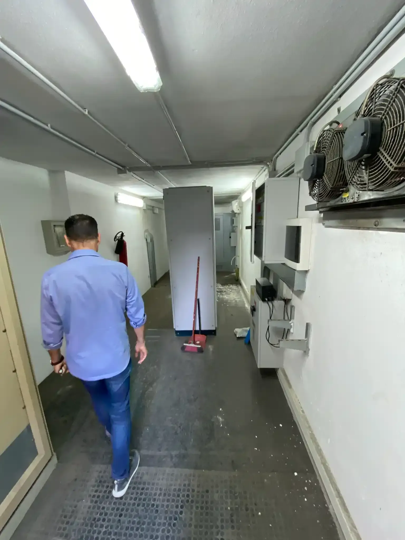 Uomo che cammina lungo uno stretto corridoio con dei macchinari e un armadietto.