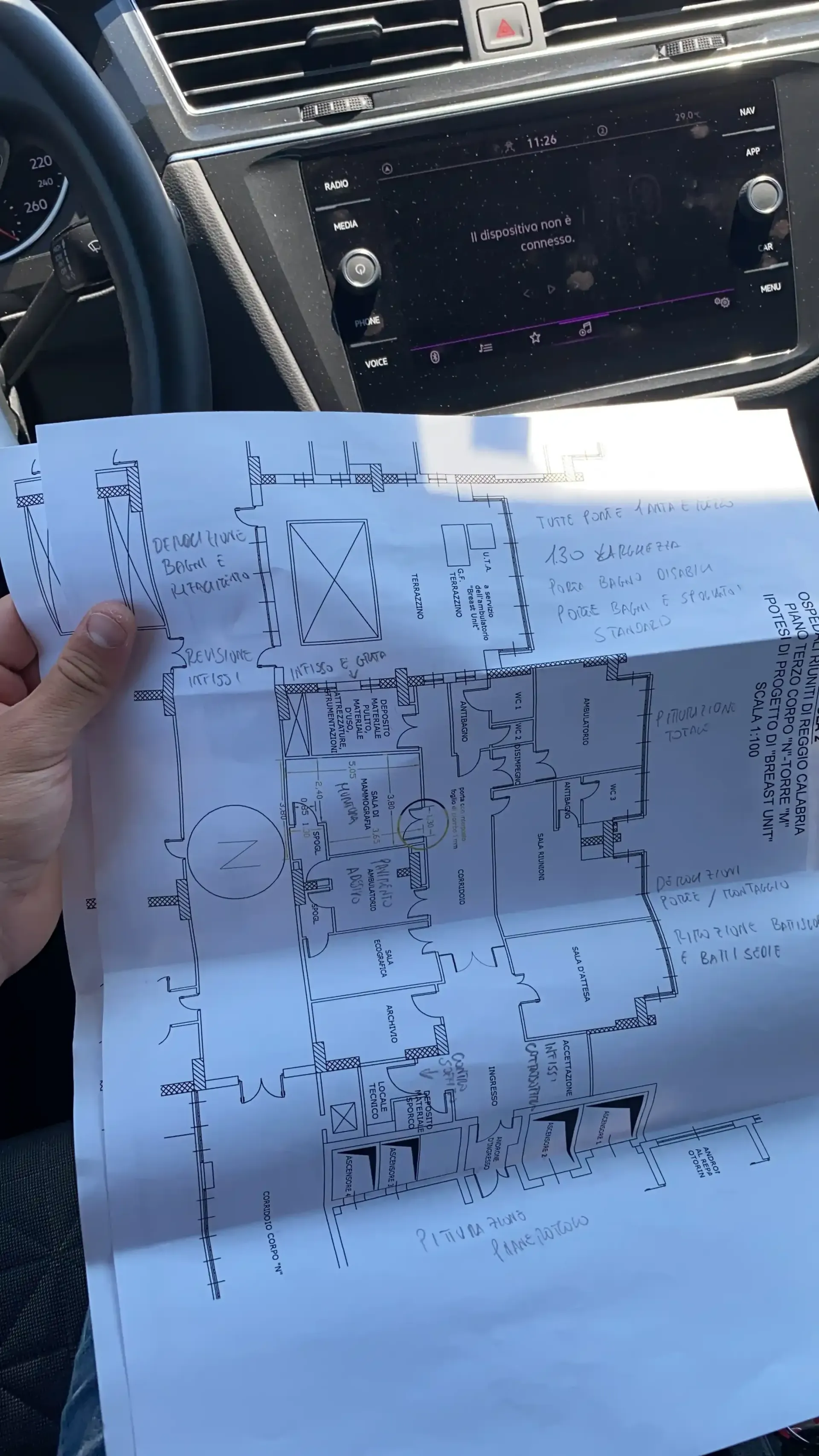 Persona che tiene in mano uno schema di circuito stampato all'interno di un'auto, con il cruscotto sullo sfondo.