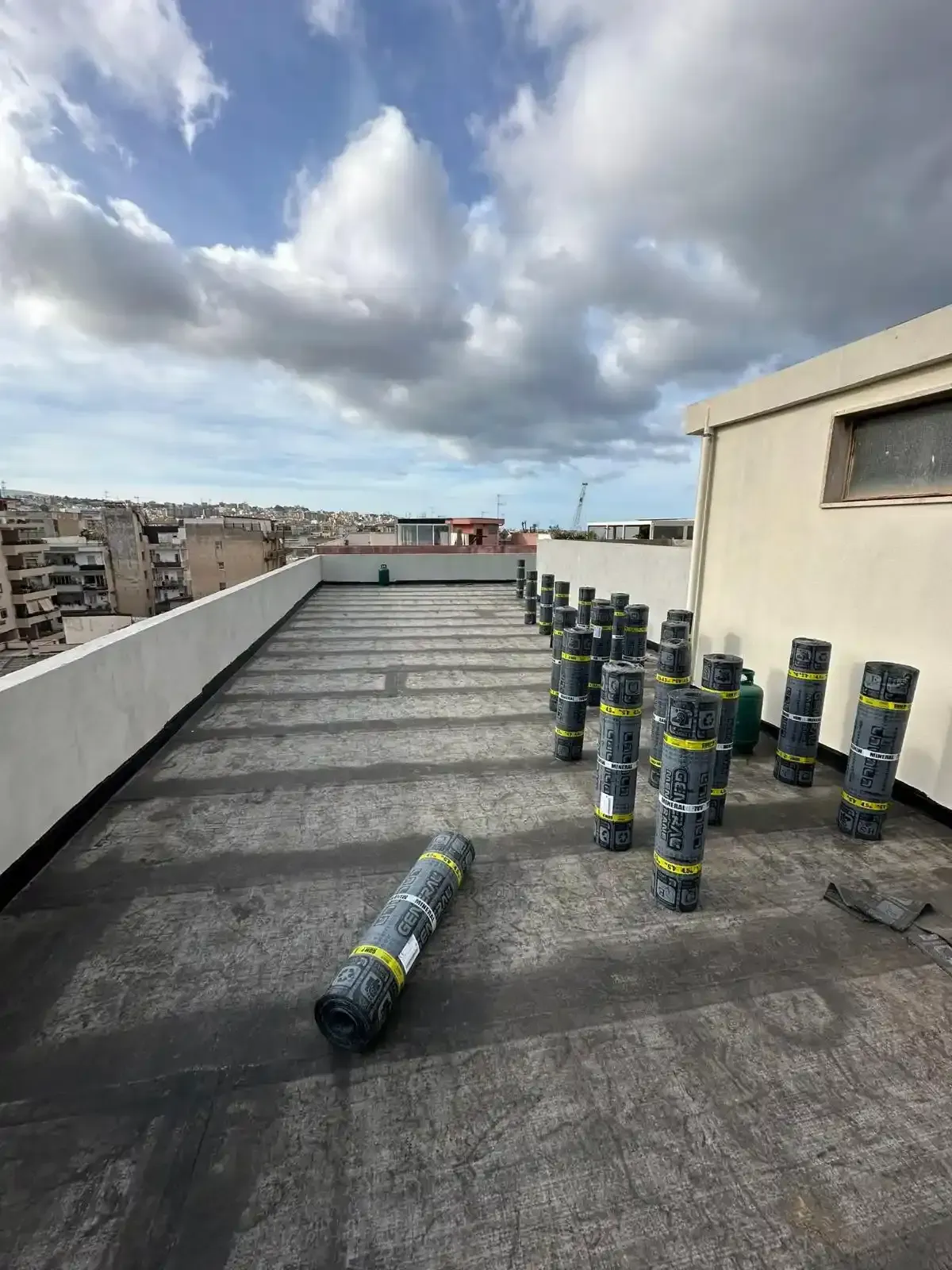 Tetto piano con materiale di copertura in rotoli. Sono visibili fasci di materiale di copertura in rotoli e edifici cittadini.
