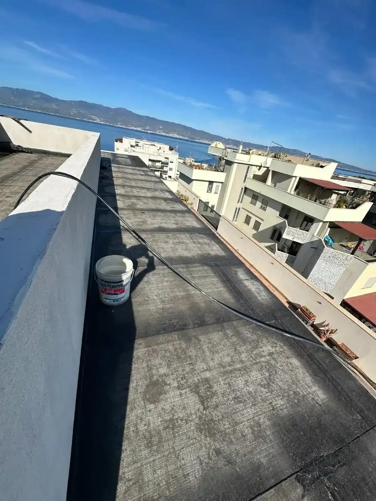 Tetto con secchio, cavi, edifici e vista sull'acqua sotto il cielo azzurro.