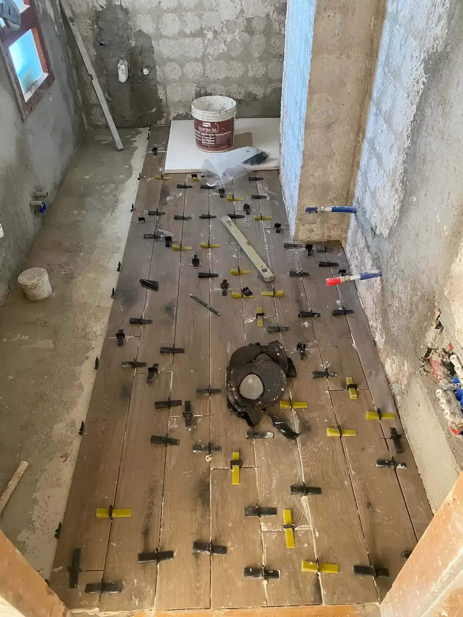 Piastrellatura del pavimento in corso con distanziatori. Piastrelle marroni, distanziatori gialli e pareti non finite.