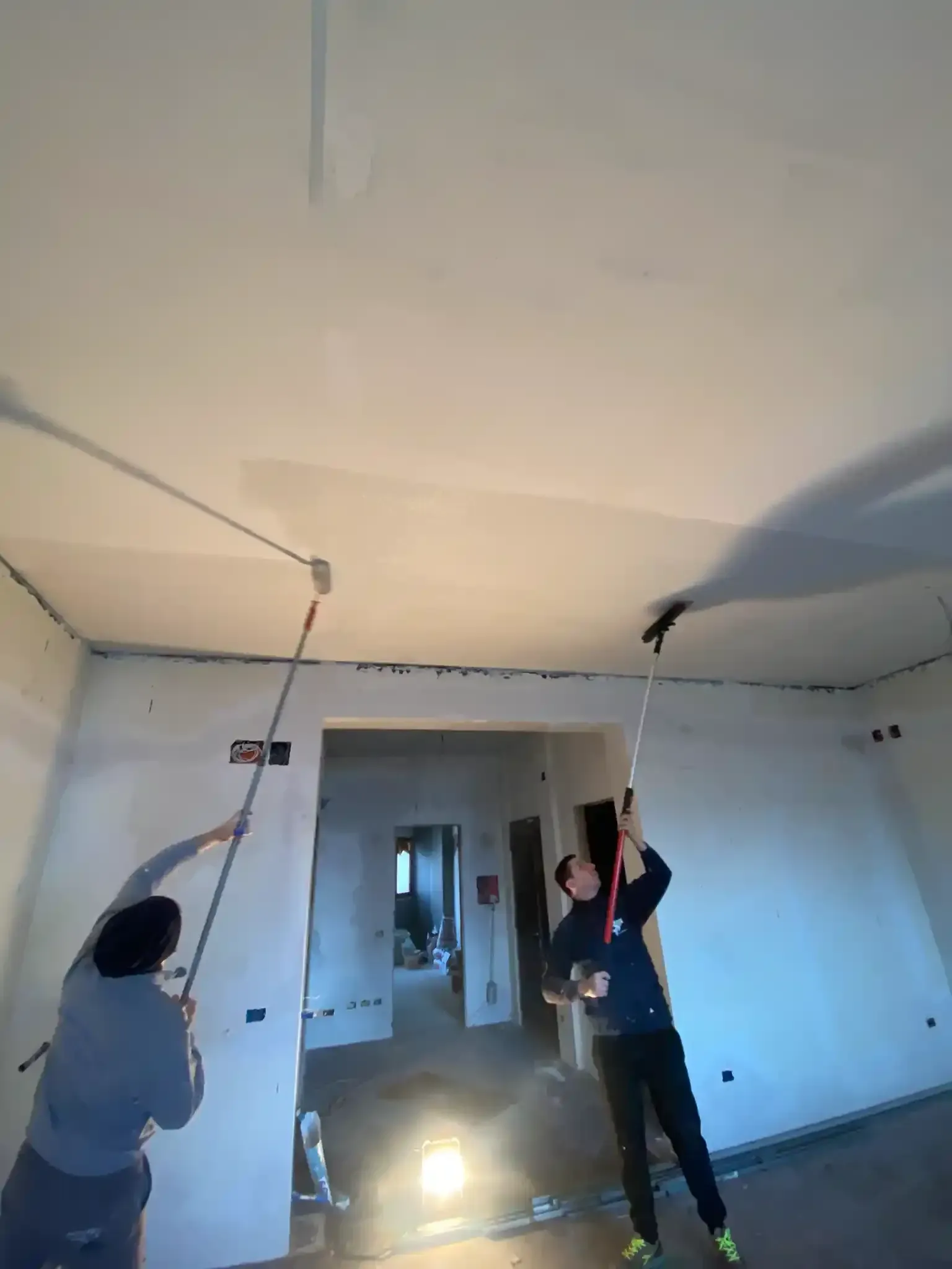 Due persone dipingono il soffitto con i rulli in una stanza non finita.