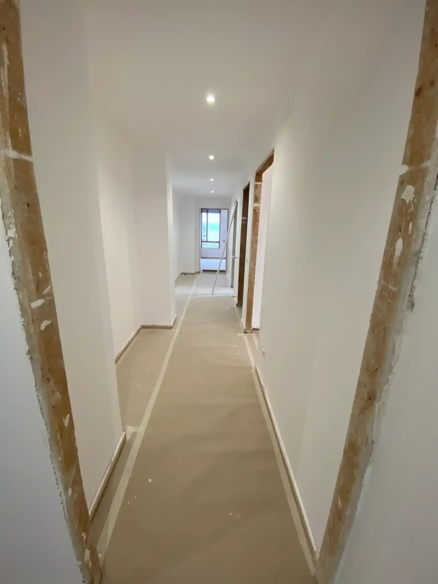 Corridoio lungo e stretto in costruzione, dipinto di bianco con cornici in legno a vista.