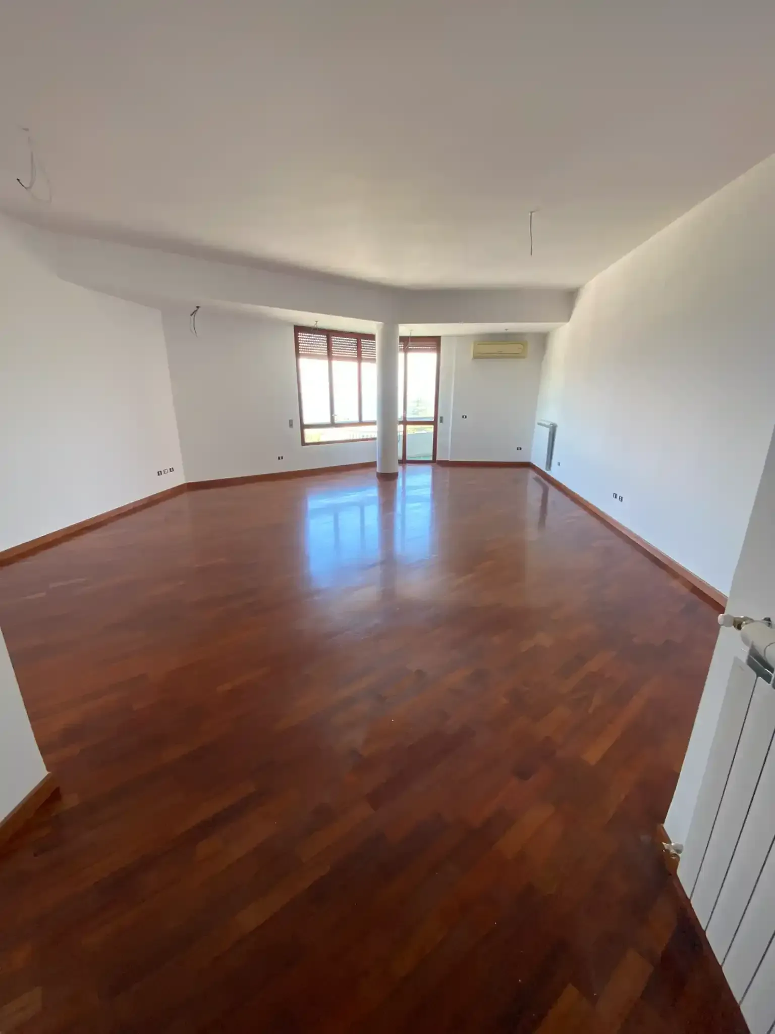 Soggiorno vuoto con pavimento in legno, pareti bianche e una finestra.