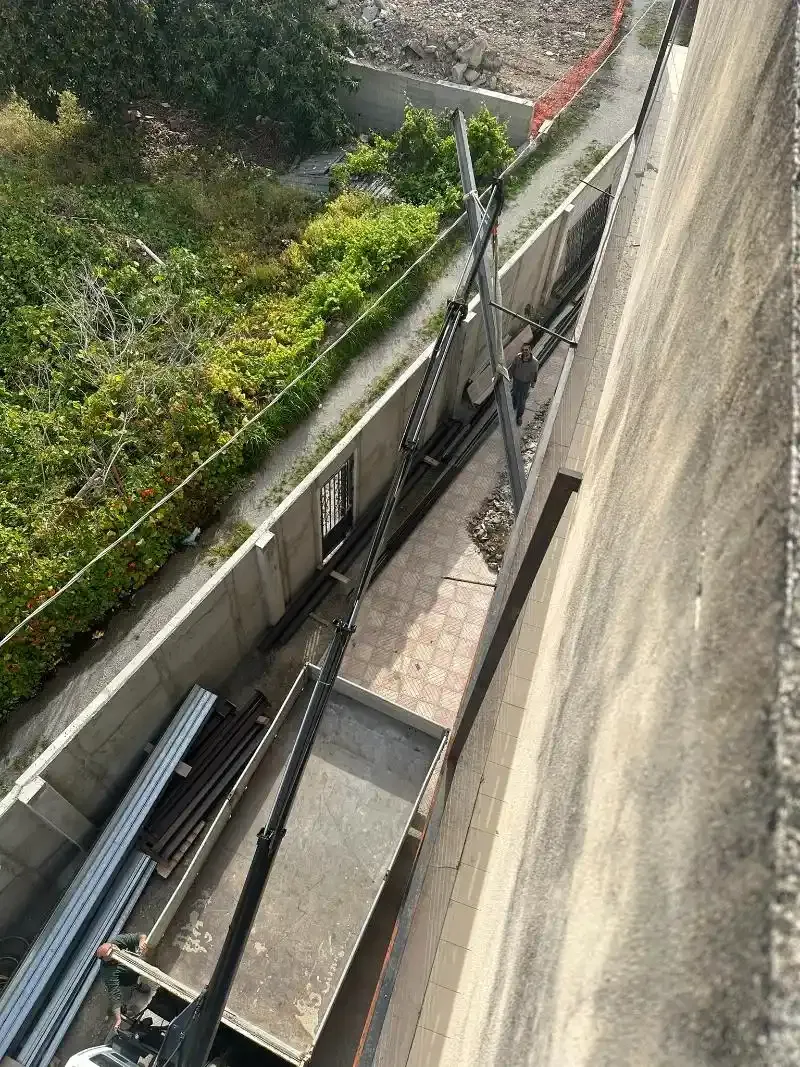 Vista di una diga in cemento con uno stretto passaggio di manutenzione, attrezzature metalliche e vegetazione.