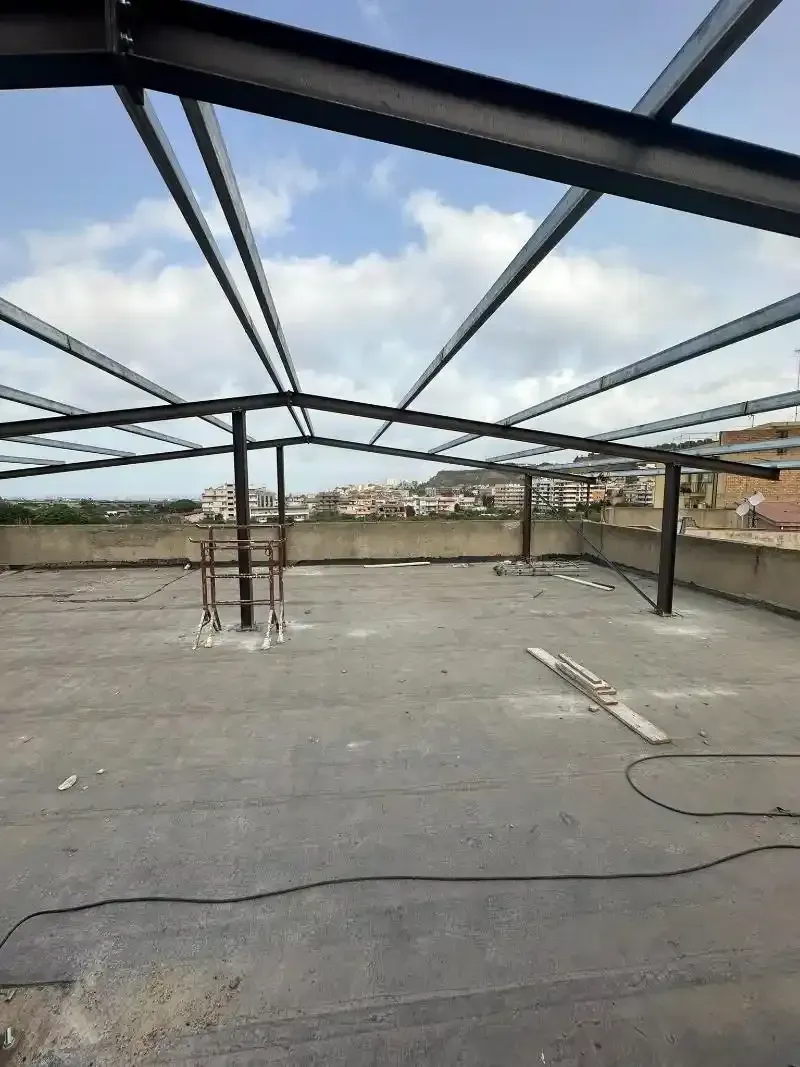 Struttura in acciaio in costruzione su un tetto con un cielo nuvoloso sullo sfondo.