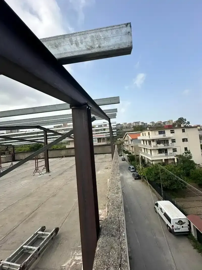 Travi d'acciaio sul tetto di un edificio, strada sottostante. Costruzione in metallo grigio e marrone contro un cielo azzurro.