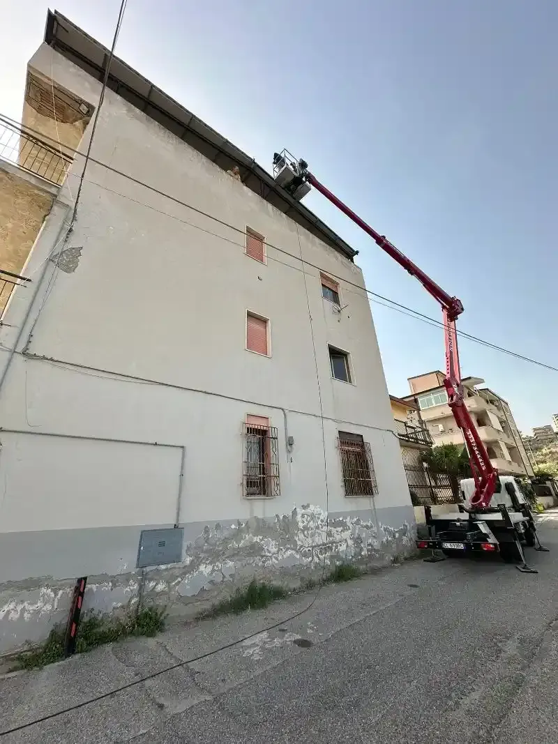 Una piattaforma aerea raggiunge la cima di un edificio bianco per le riparazioni in una giornata di sole.
