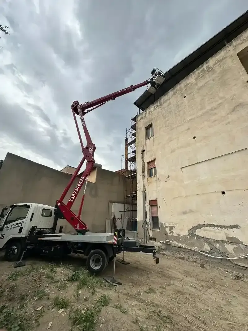 Un camion a piattaforma si protende verso un edificio. Qualcuno lavora sulla piattaforma, sotto un cielo nuvoloso.