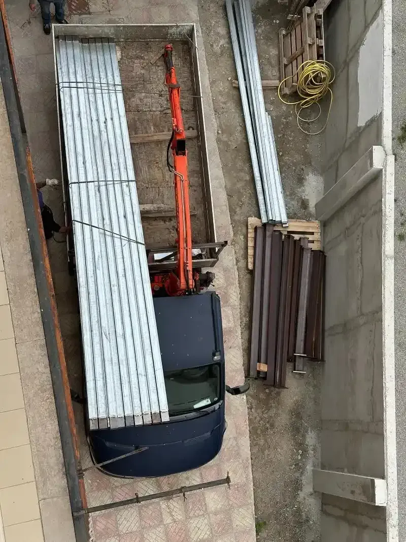 Vista dall'alto di un piccolo escavatore in uno stretto cantiere, circondato da materiali da costruzione.