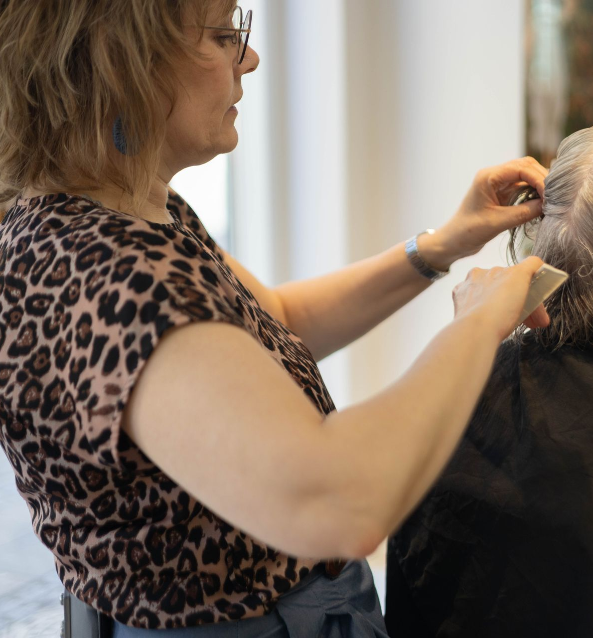 Kvinde i en leopardprintet top stylerer en klients hår i en salon