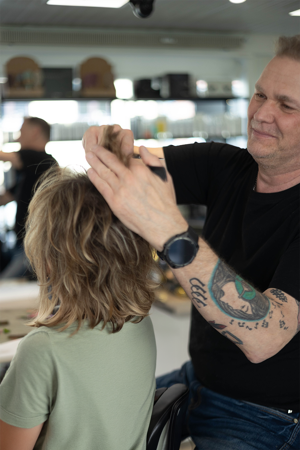 Stylist klipper en klients hår i en salon med en saks og kam synlige.