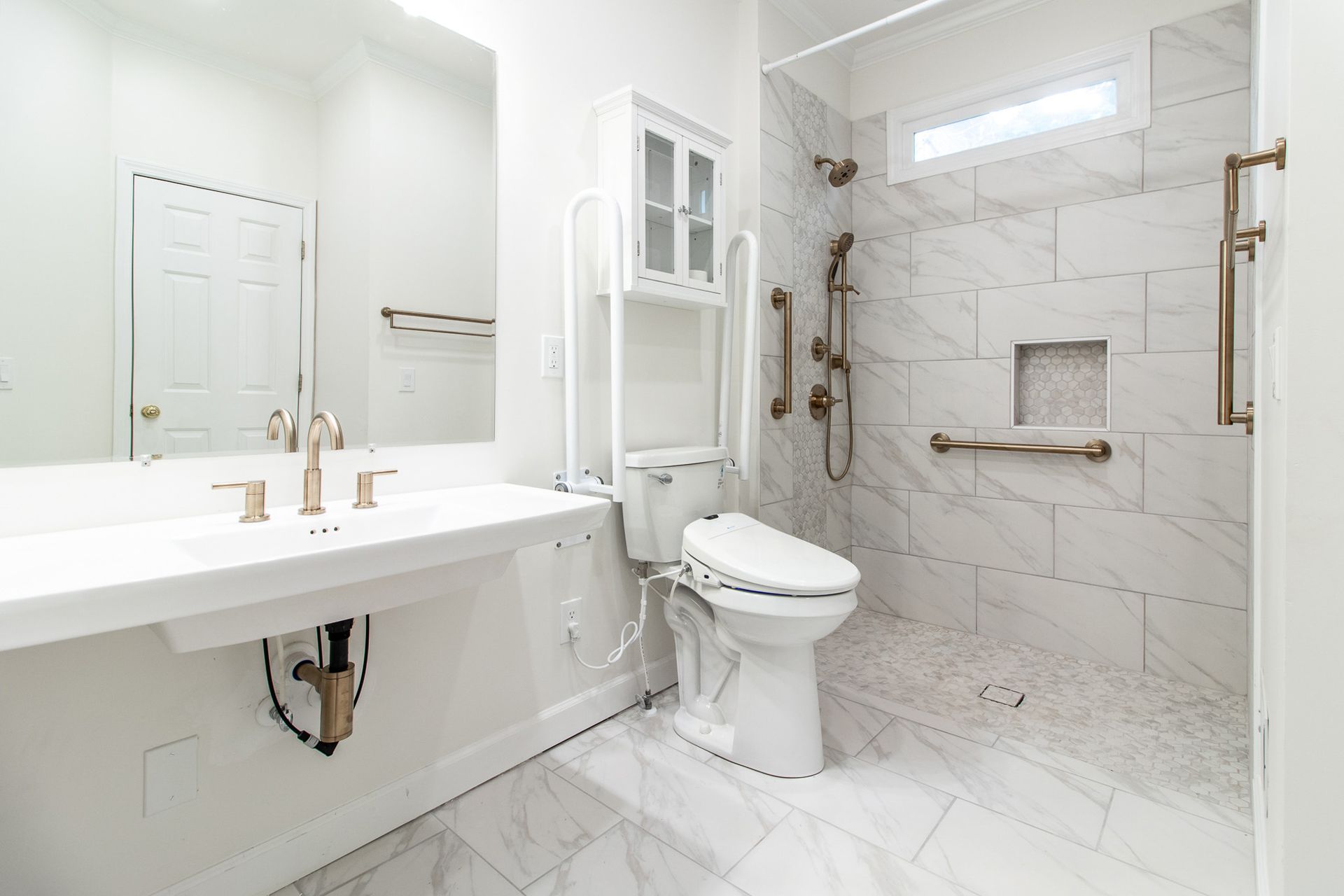Accessible bathroom with white marble, grab bars, roll-under sink, and a shower with built-in bench.