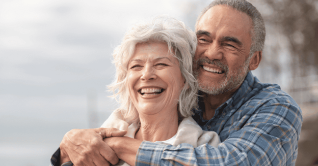 Two people embracing and smiling while looking off to the side outdoors.