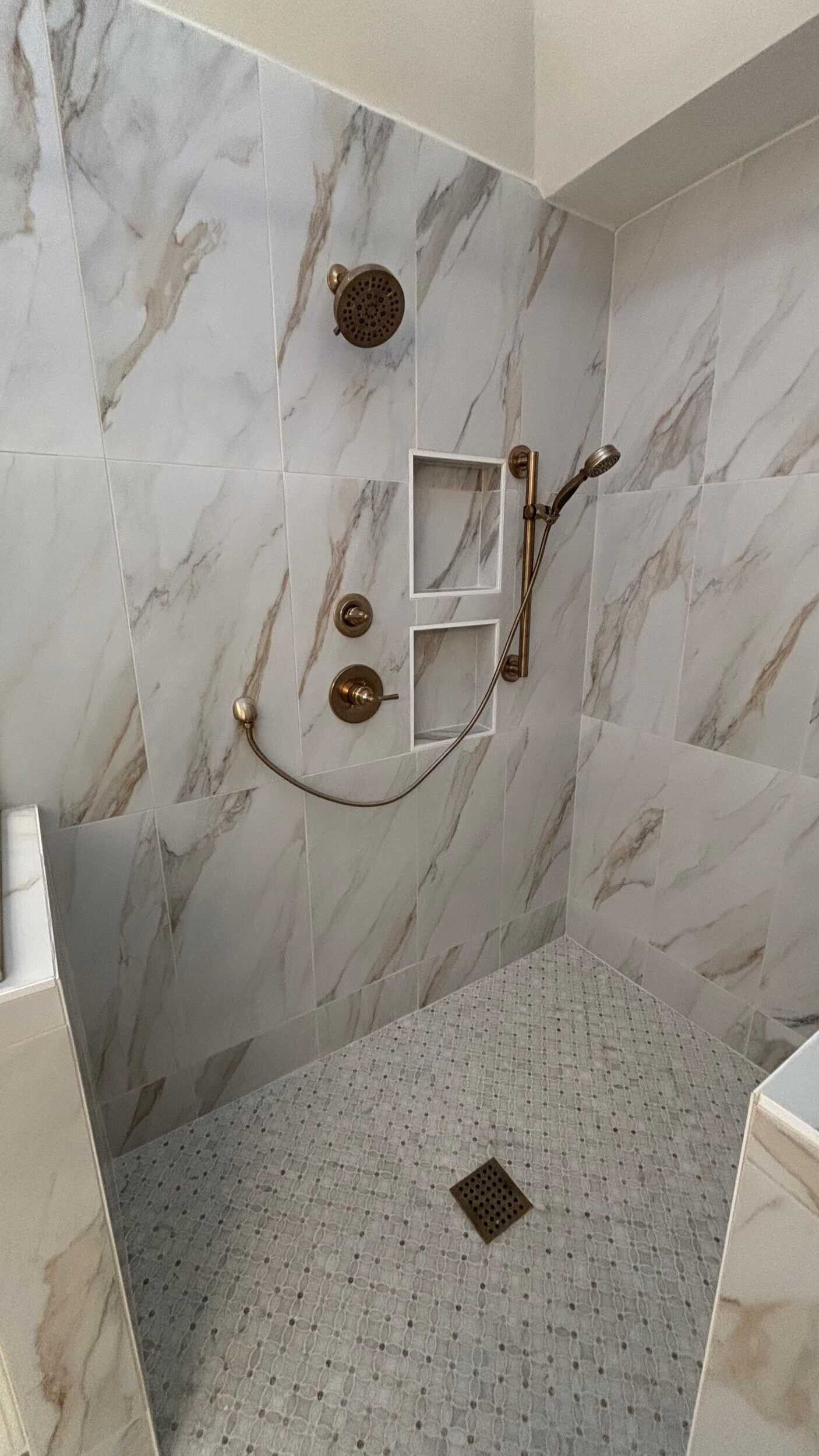 Marble-tiled shower with gold fixtures and mosaic floor. Recessed shelves hold shower essentials.