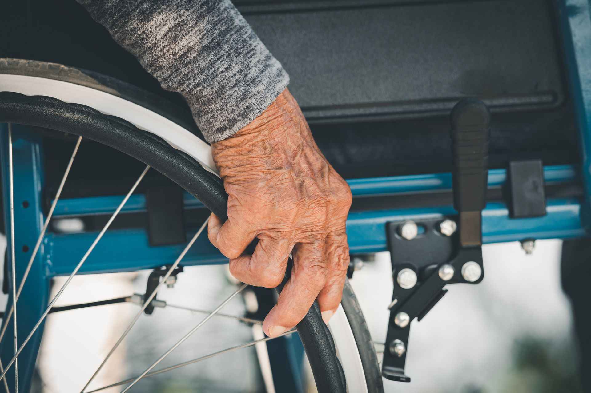 A person's hand on a wheelchair wheel; close-up of wrinkled skin, blue chair.