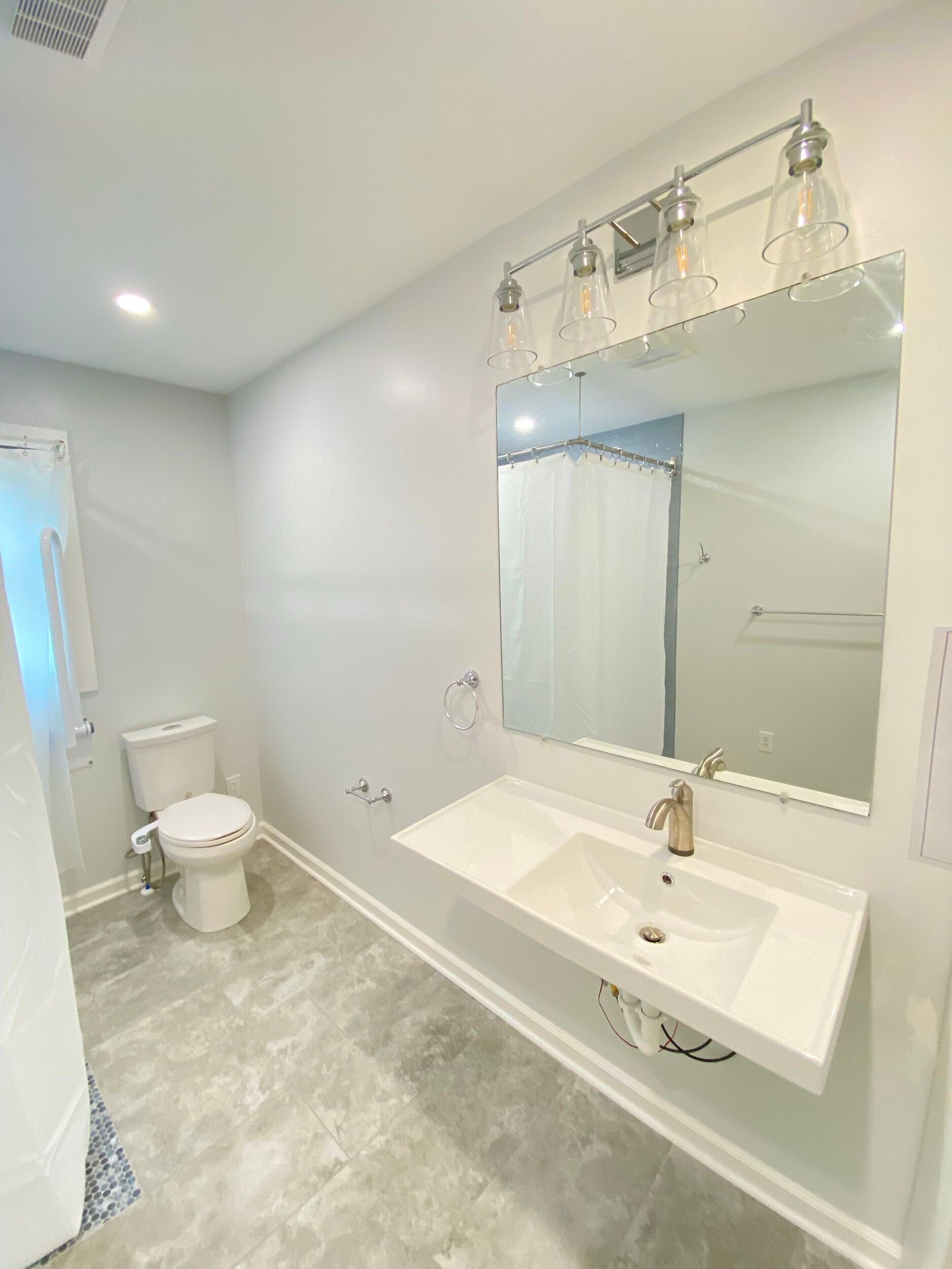 Bathroom with a floating vanity, toilet, and large mirror with a light fixture.