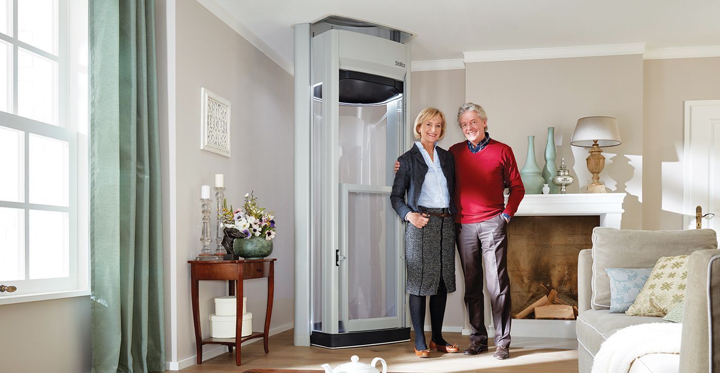 A man and a woman are standing in a living room next to a lift.