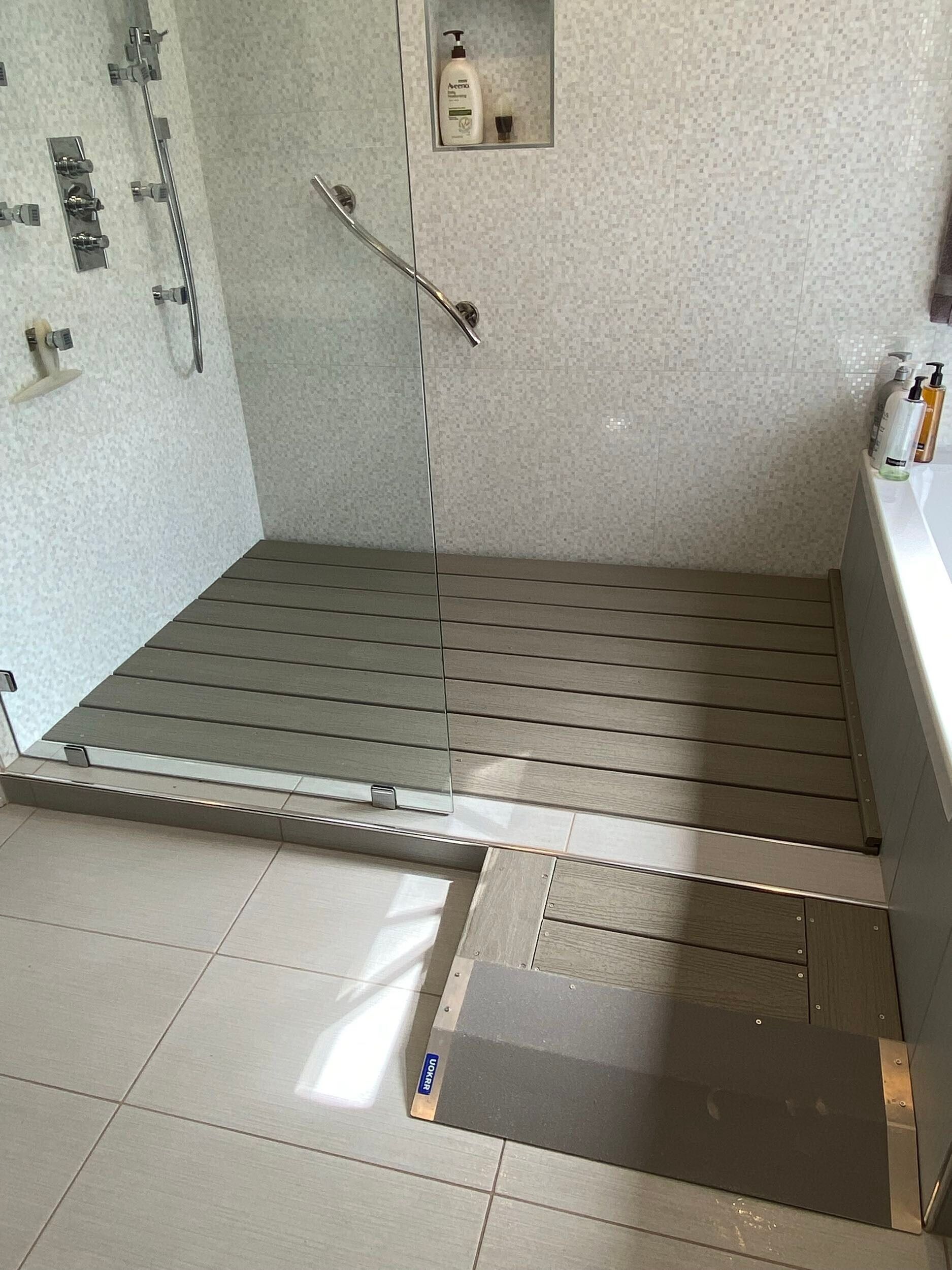 Accessible shower with fold-down seat, grab bars, and tiled floor in a bathroom.