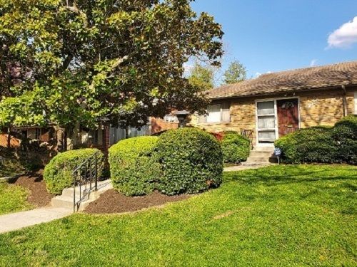 a brick house with a lush green lawn and bushes in front of it .
