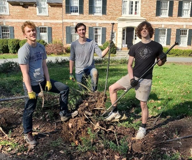 three young men are standing in front of a large pile of dirt .