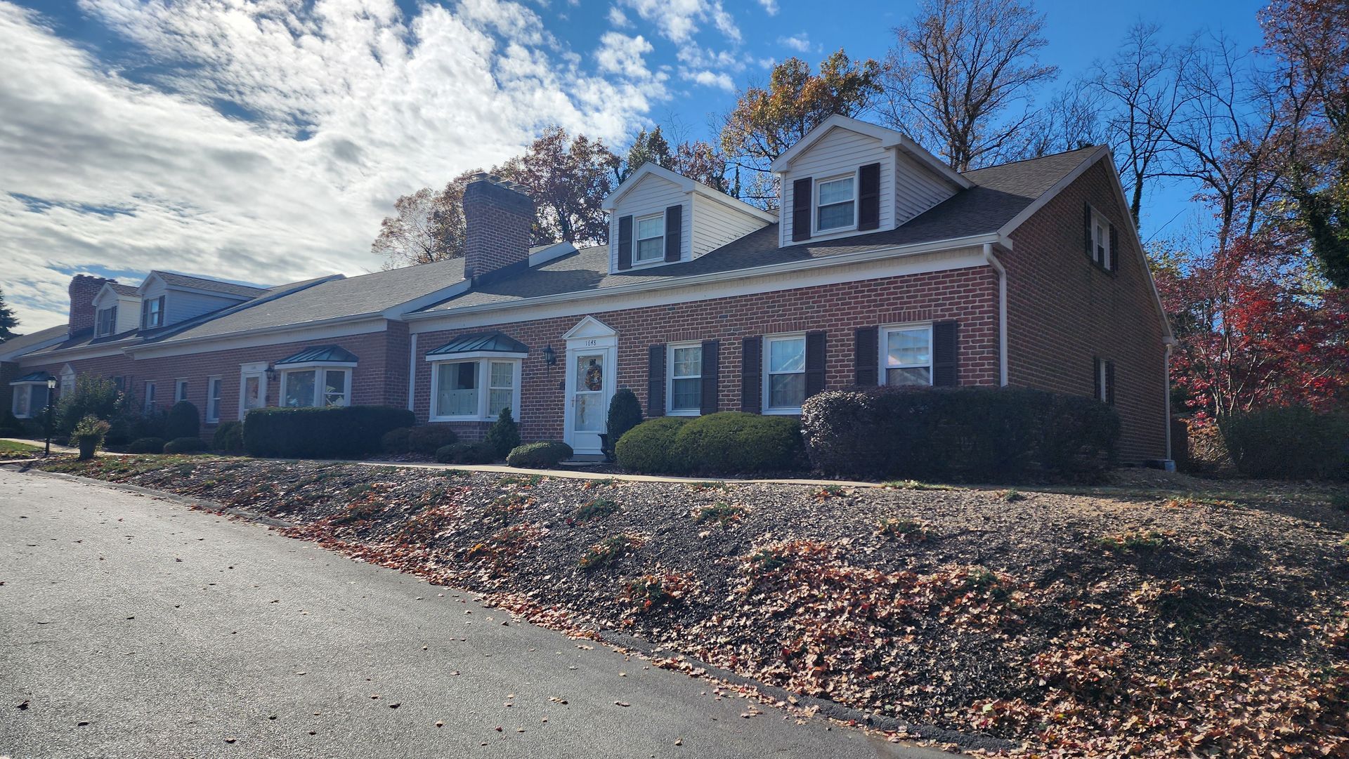 A large brick house with a lot of leaves on the ground in front of it