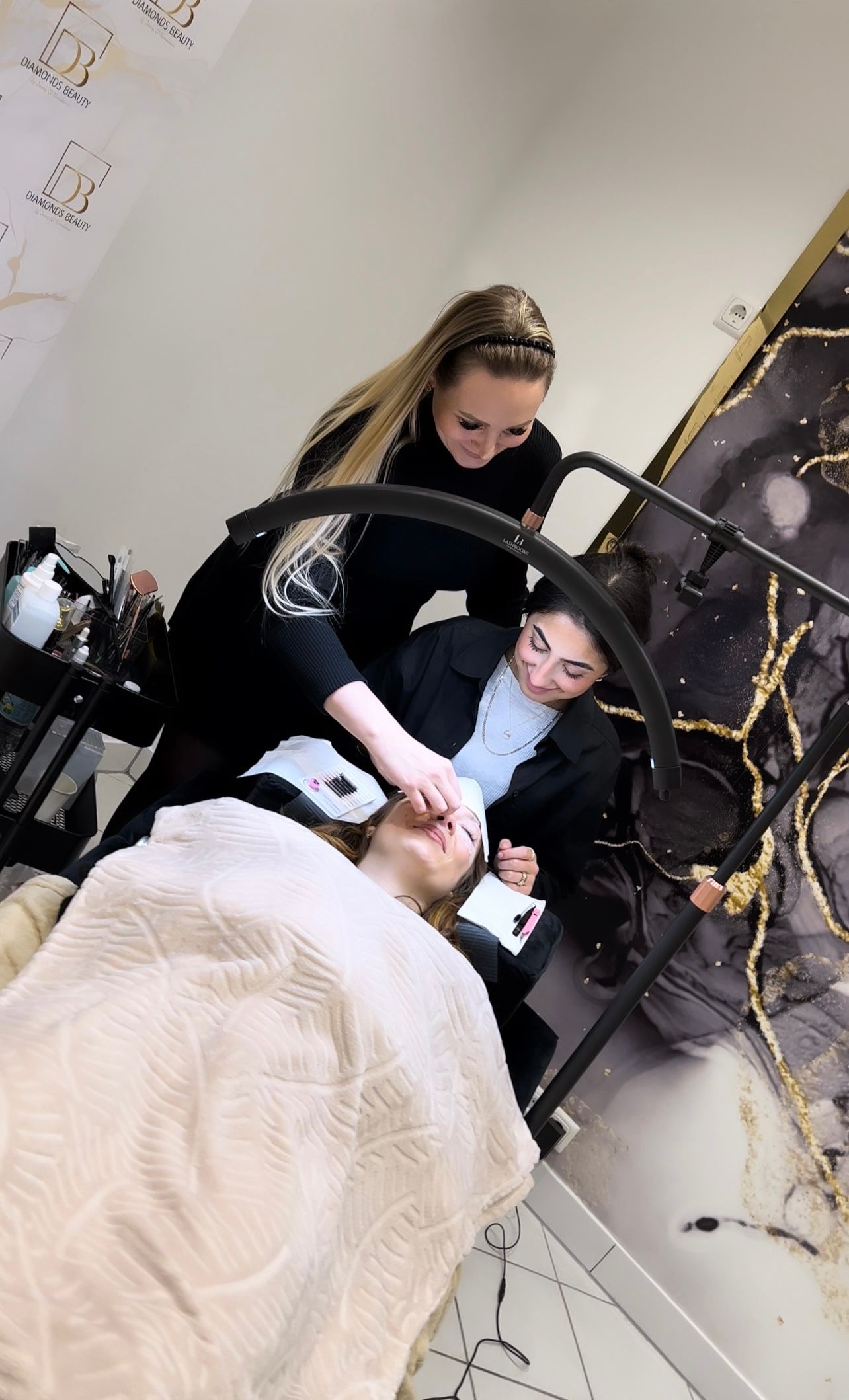 Zwei Frauen arbeiten in einem Salon an den Wimpern einer Frau