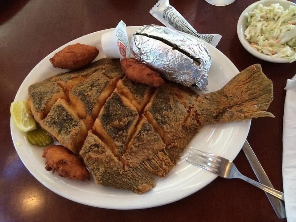 A white plate topped with fried fish a baked potato and coleslaw