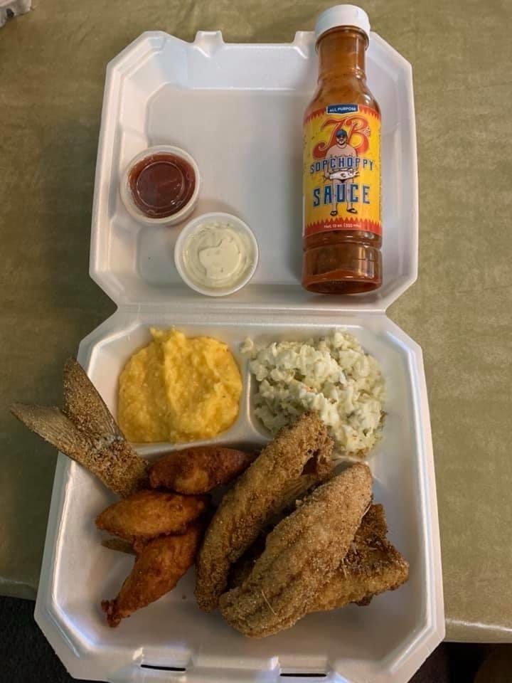 A styrofoam container filled with food and a bottle of sauce.