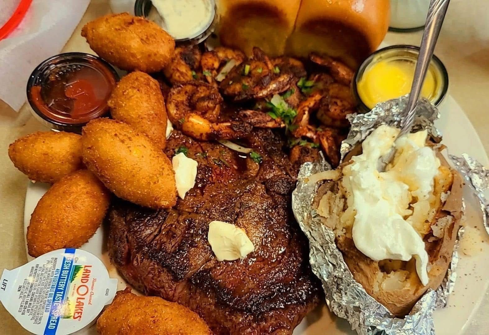 A plate of food with a steak , shrimp , corn on the cob and a baked potato.
