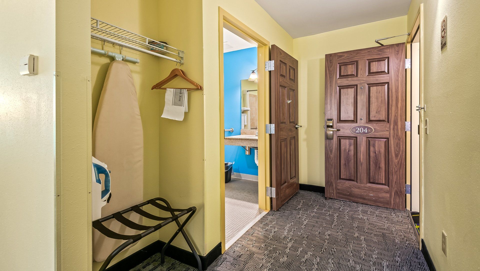 A hotel room with a closet , ironing board , and luggage rack.