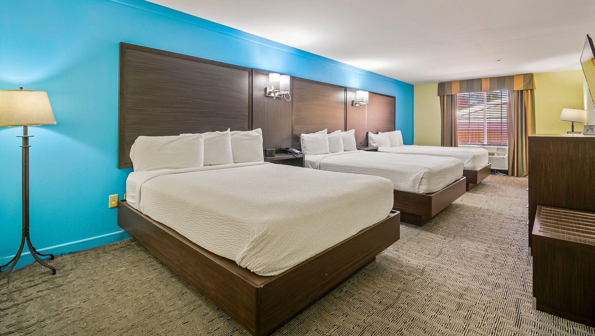 A hotel room with three beds and a blue wall.