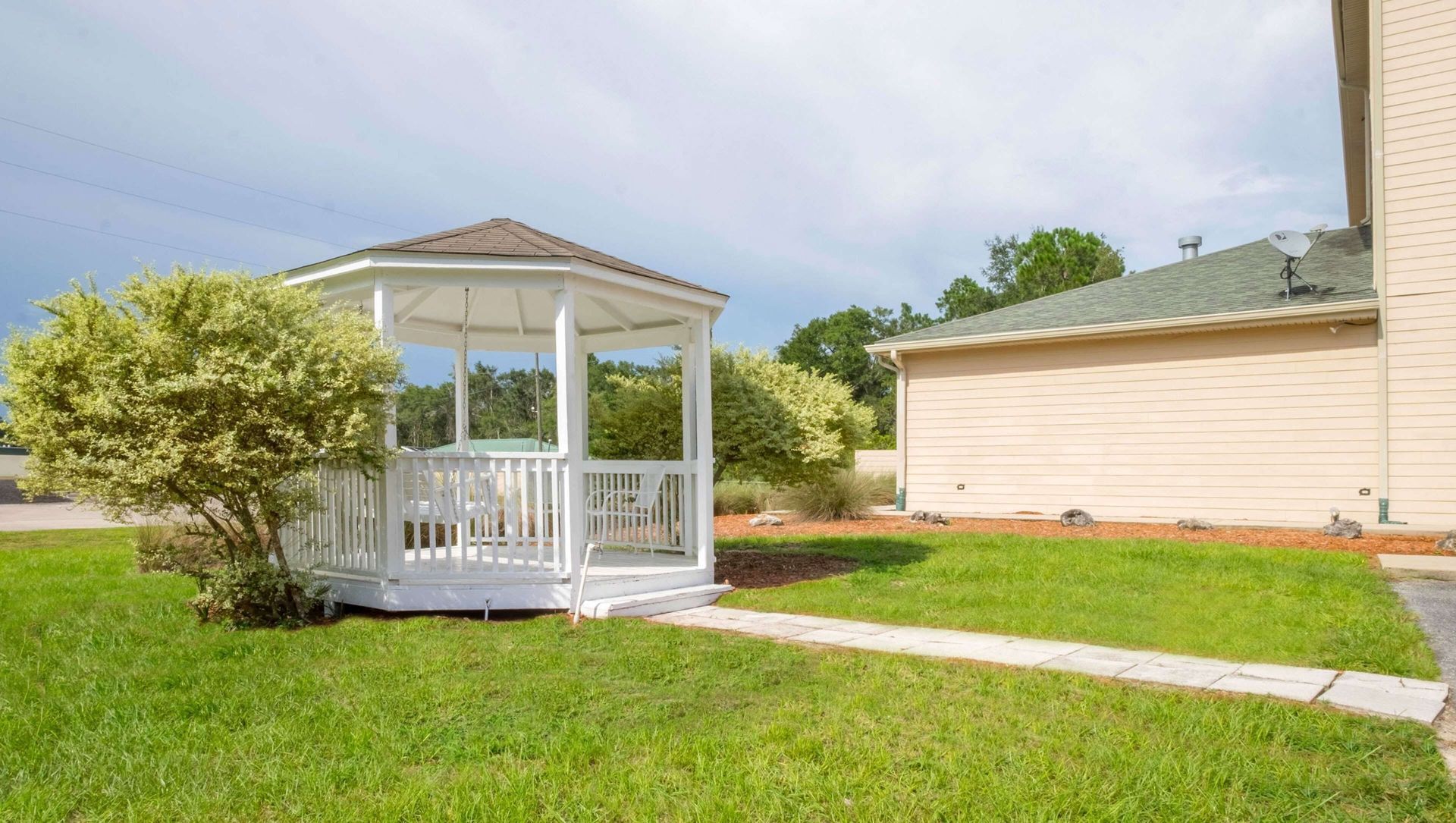A white gazebo is sitting in the middle of a lush green lawn in front of a house.