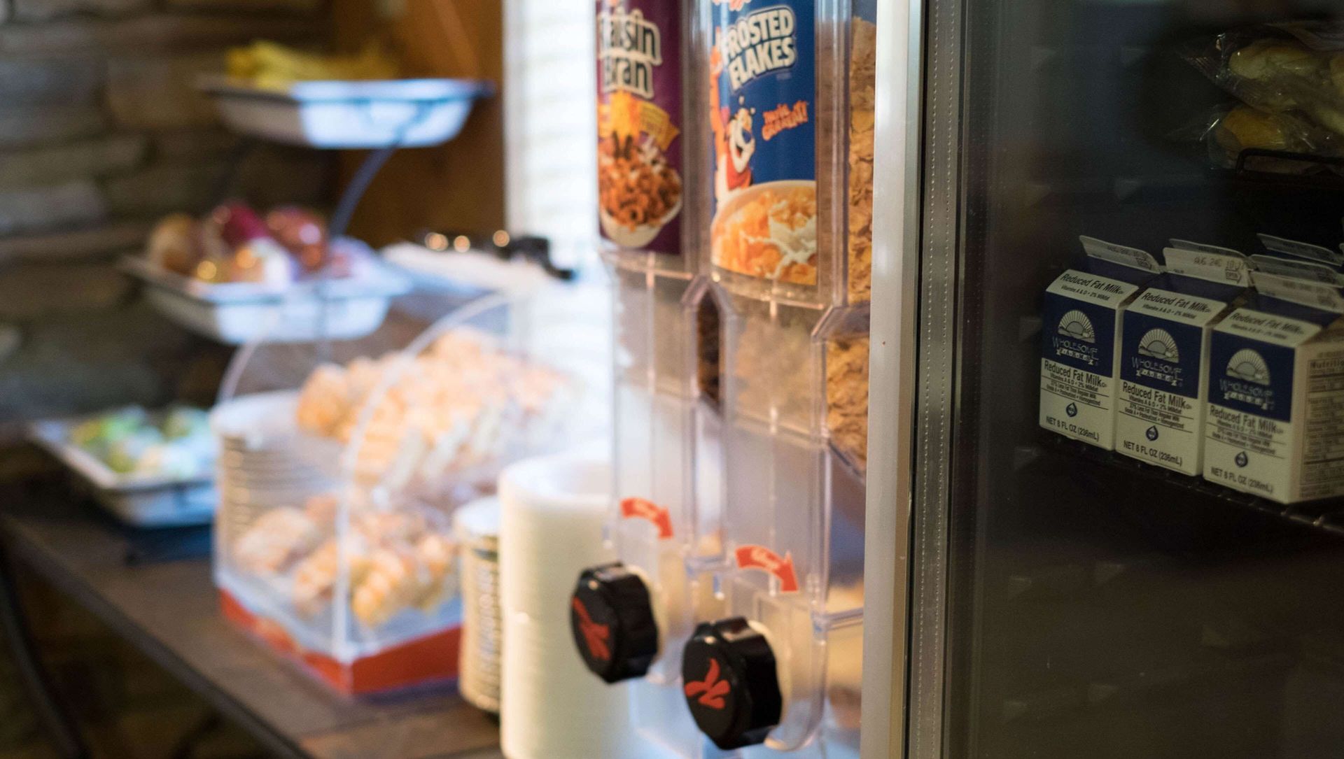 A buffet table with a dispenser of cereal and milk.