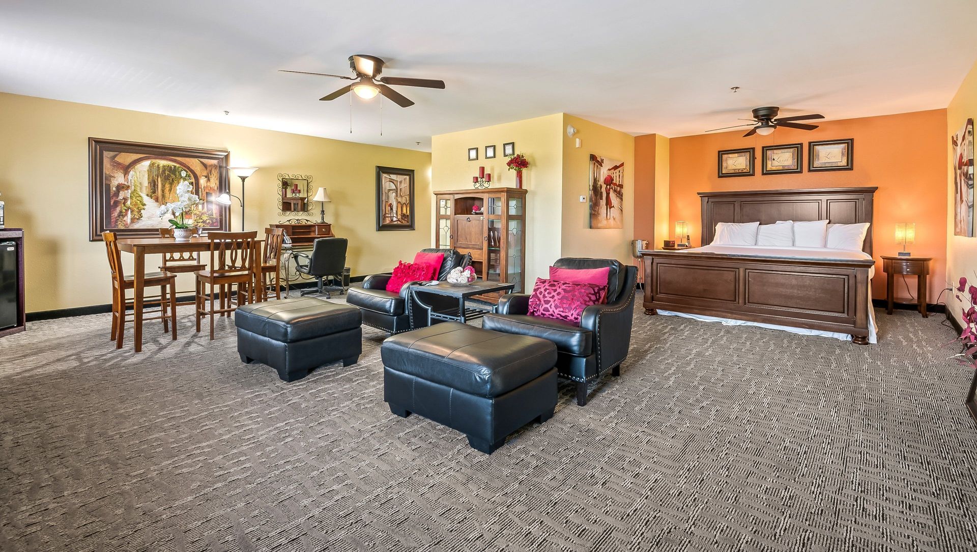 A living room with a king size bed , chairs , ottomans and a table.