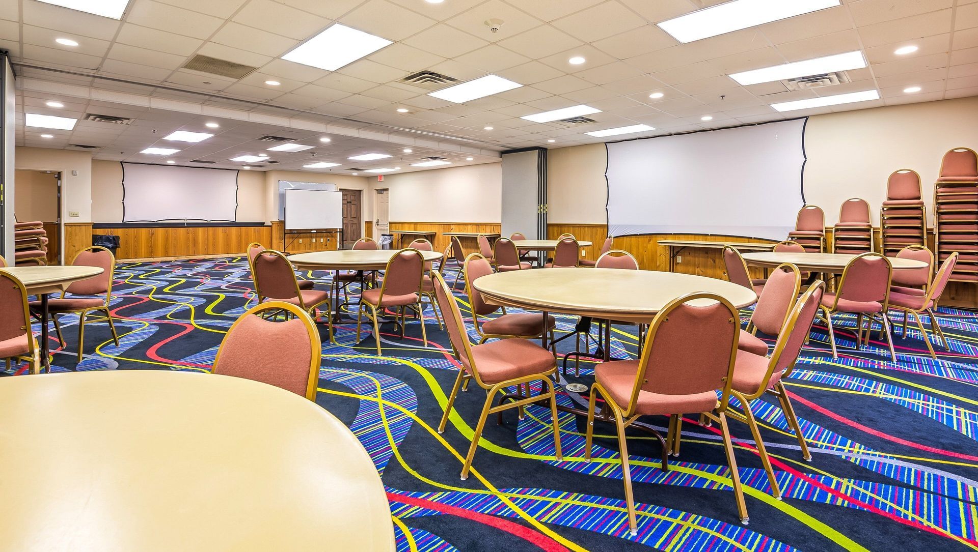 A large conference room with tables and chairs and a projector screen.