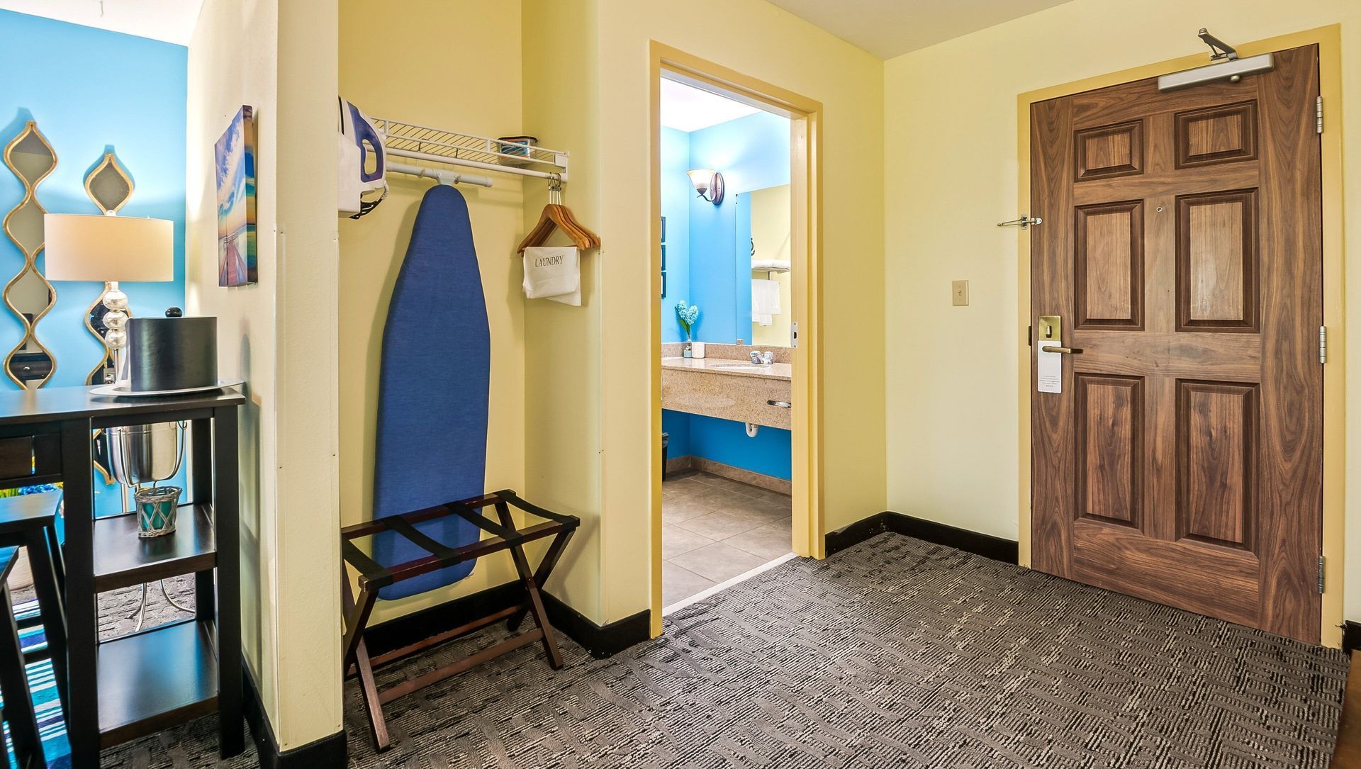 A hotel room with a wooden door and a blue ironing board.